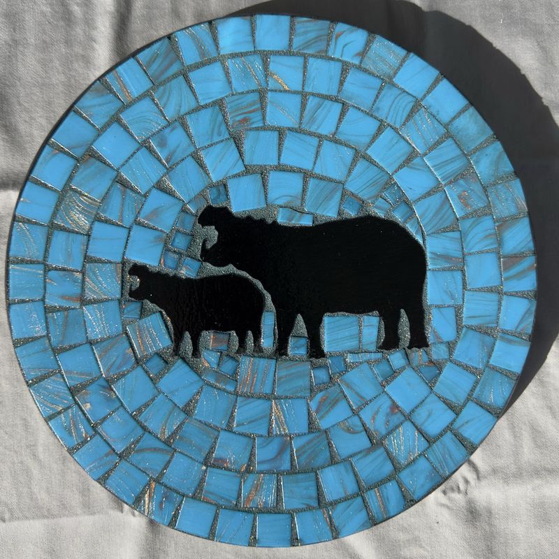 Round mosaic wall plate with two black hippo silhouettes on a sky-blue marbled glass background
