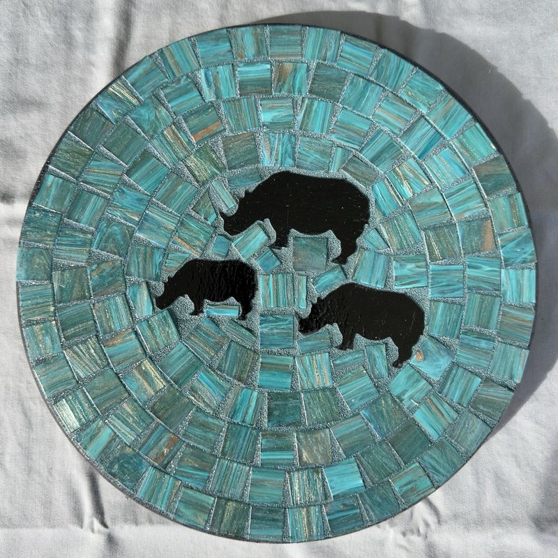 Round mosaic wall plate with three black rhino silhouettes on a turquoise glass background