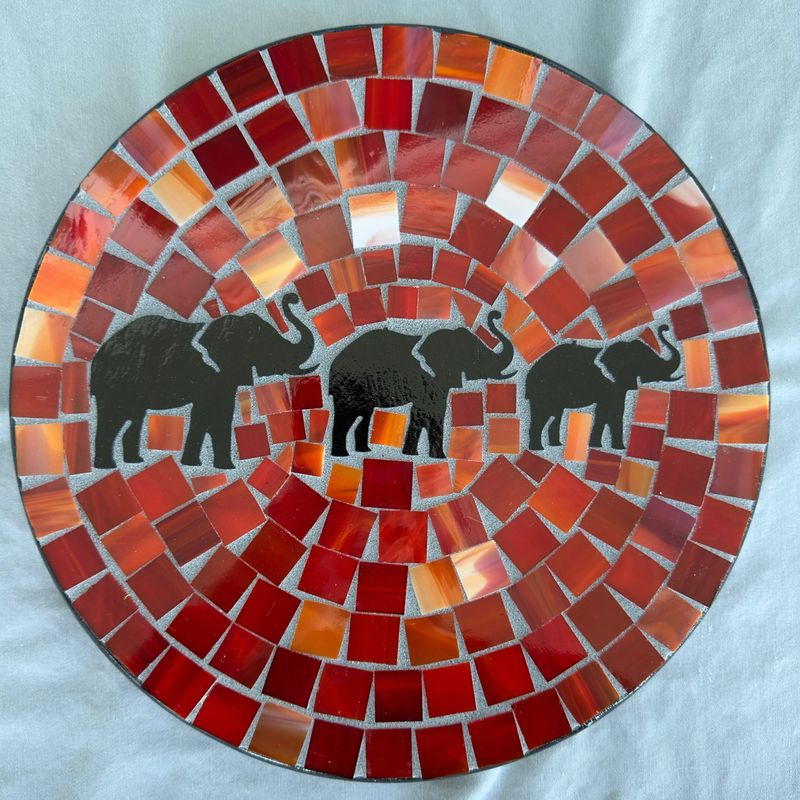 Round mosaic wall plate featuring three elephant silhouettes on a vivid red tessera background