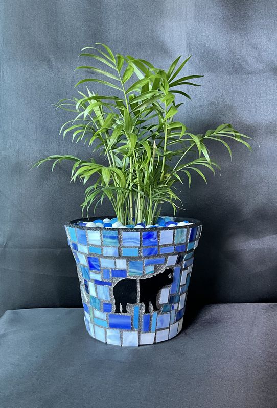 Tapered round planter in blue and white mosaic with a black rhino silhouette, parlor palm inside