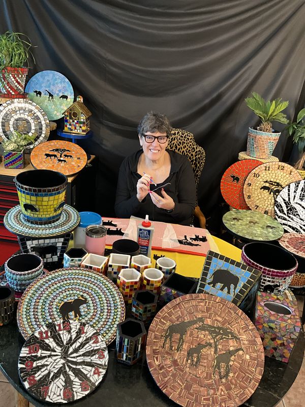 Janet Girdwood-Naddell at her Austin studio worktable, surrounded by finished mosaic plates, clocks, and planters