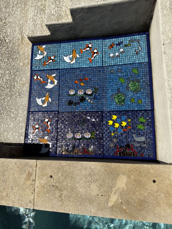 Custom mosaic panels installed in a space beside a pool, featuring koi, turtles, and tropical fish in blue glass tile