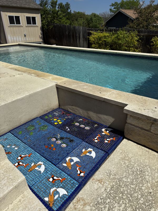 Angled view of a custom mosaic panel installed on the pool deck, with the water visible in the background