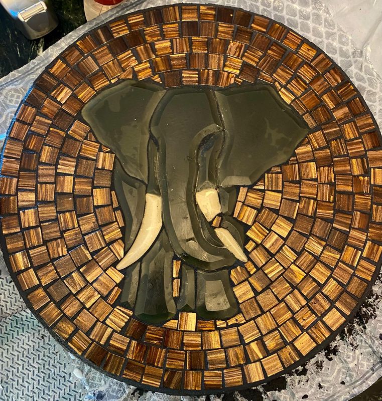 Work-in-progress of a three-dimensional elephant-head mosaic on a round plate, with glue visible
